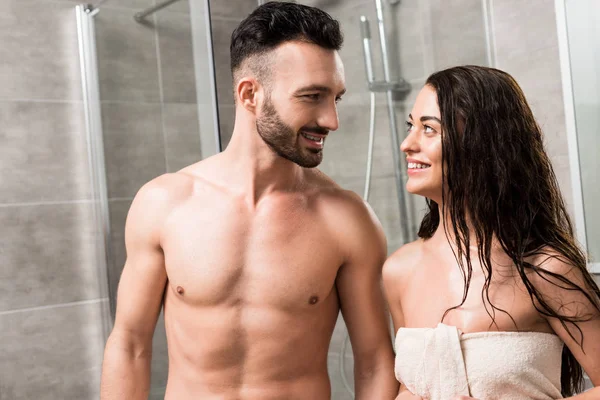 Fröhlicher bärtiger Mann schaut lächelnde brünette Frau im Badezimmer an — Stockfoto