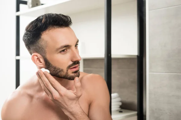 Homem barbudo bonito aplicando espuma de barbear no rosto no banheiro — Fotografia de Stock