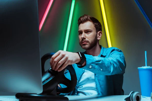 Selective focus of handsome and good-looking man playing video game with steering wheel — Stock Photo