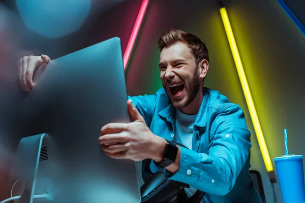 Foco seletivo de homem bonito e feliz sorrindo e segurando monitor de computador — Fotografia de Stock