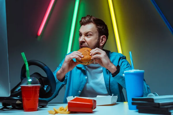 Bonito e bonito jovem adulto homem comendo hambúrguer e olhando para longe — Fotografia de Stock