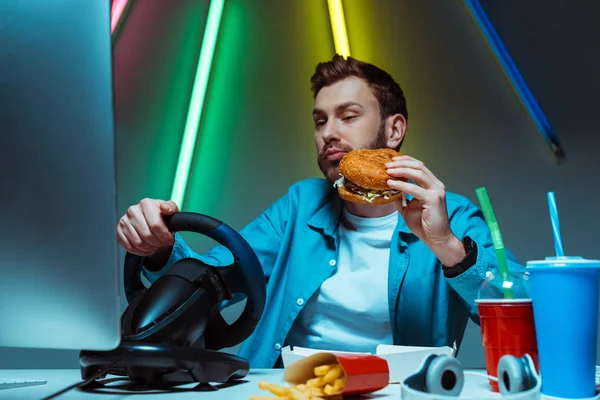 Enfoque selectivo de guapo deportista cibernético comer hamburguesa y jugar juego de ordenador - foto de stock