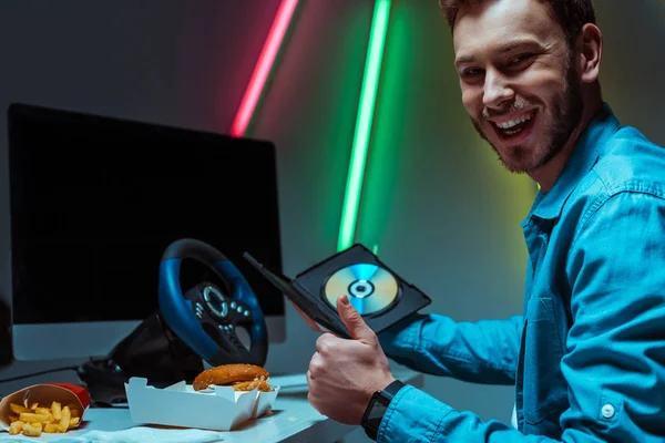 Uomo bello e sorridente in possesso di compact disk con videogioco e mostrando come — Foto stock