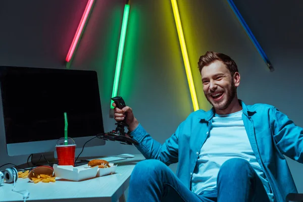 Smiling and handsome cyber sportsman holding joystick and looking away — Stock Photo