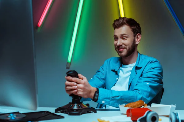 Schöner und lächelnder Mann spielt Videospiel mit Steuerknüppel und schaut auf Computermonitor — Stockfoto