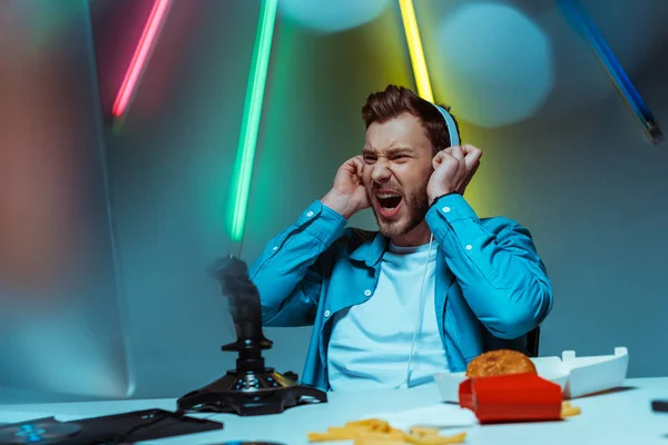 Angry and handsome cyber sportsman in headphones looking at computer monitor — Stock Photo
