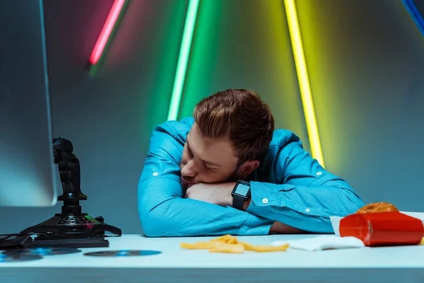 Schöner junger erwachsener Mann schläft und ruht auf Tisch mit Steuerknüppel und Fast Food — Stockfoto