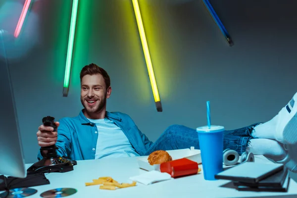 Handsome cyber sportsman playing video game with joystick and looking at computer monitor — Stock Photo