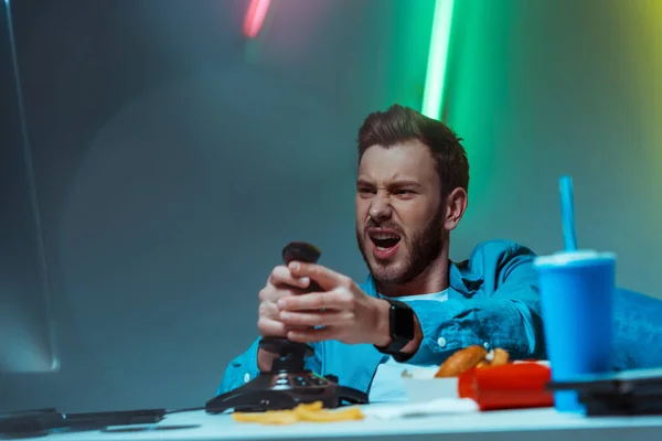 Selective focus of handsome and angry man playing video game with joystick — Stock Photo