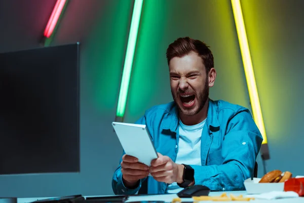 Hombre guapo y enojado sosteniendo el teclado de la computadora y gritando - foto de stock