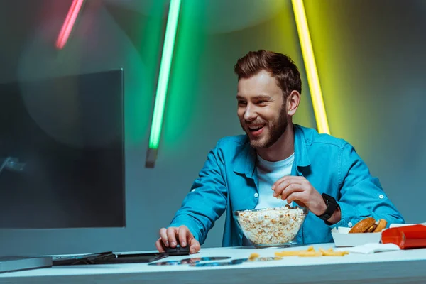 Uomo bello e sorridente che tiene il mouse del computer e mangia popcorn — Foto stock