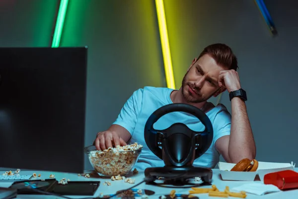 Schöner und trauriger Mann schaut auf Computermonitor und isst Popcorn — Stockfoto