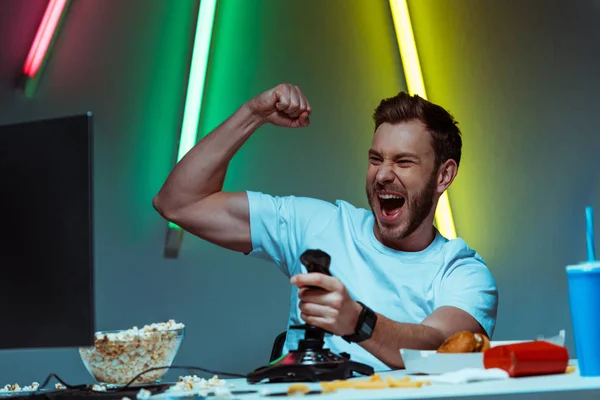 Apuesto deportista cibernético jugando videojuego con joystick y mostrando sí gesto - foto de stock