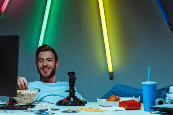 Schöner und lächelnder Mann, der auf Computerbildschirm schaut und Popcorn isst — Stockfoto