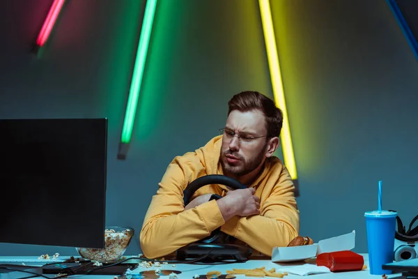 Hombre guapo y guapo en gafas sosteniendo el volante y mirando el monitor de la computadora - foto de stock