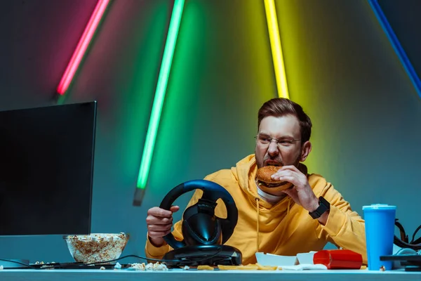 Handsome and good-looking man in glasses playing with steering wheel and eating burger — Stock Photo