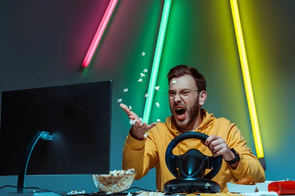 Angry and good-looking man in glasses playing with steering wheel and throwing popcorn — Stock Photo