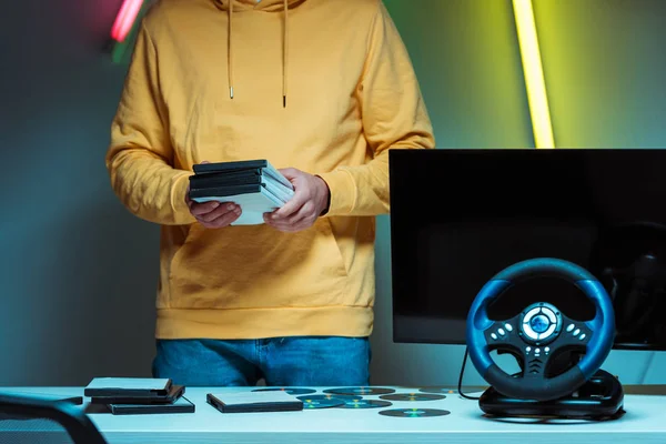 Cropped view of man standing and holding compact disks with video games — Stock Photo