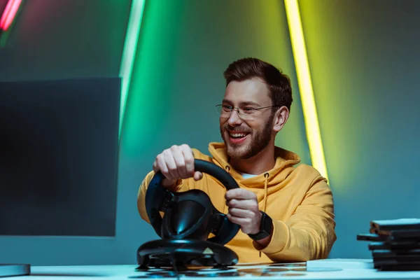 Lächelnder und gutaussehender Mann mit Brille spielt Videospiel mit Lenkrad — Stockfoto