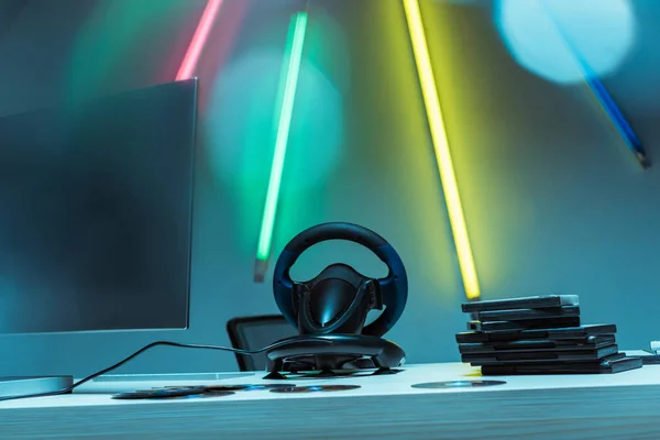 Computer monitor, steering wheel and compact disks with video games on table — Stock Photo