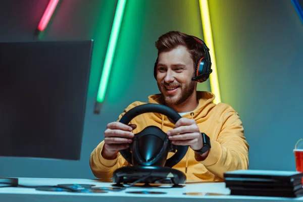 Young adult and handsome man in headphones playing video game with steering wheel — Stock Photo