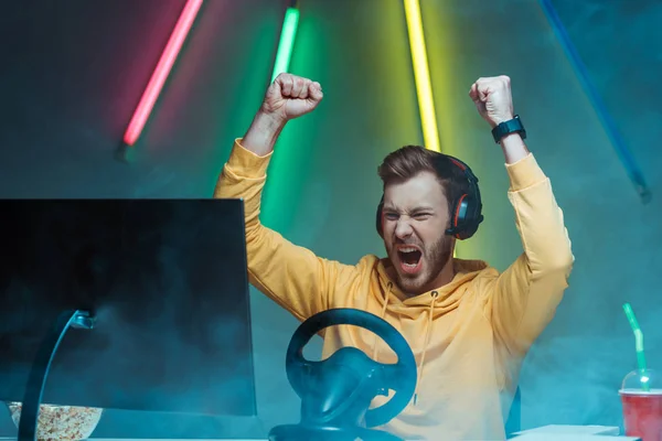 Young adult and handsome man in headphones playing video game and showing yes gesture — Stock Photo