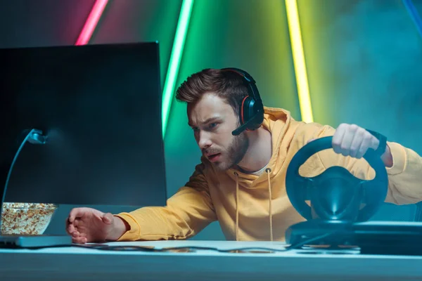 Young adult and handsome man in headphones playing video game with steering wheel — Stock Photo