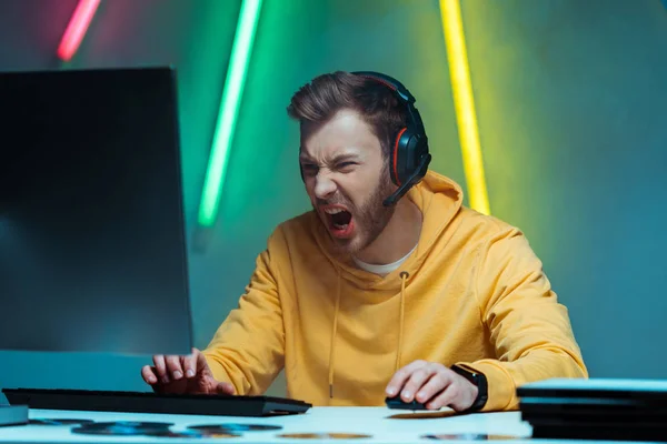 Wütender und gutaussehender Mann mit Kopfhörern spielt Videospiel mit Computermaus und Tastatur — Stockfoto