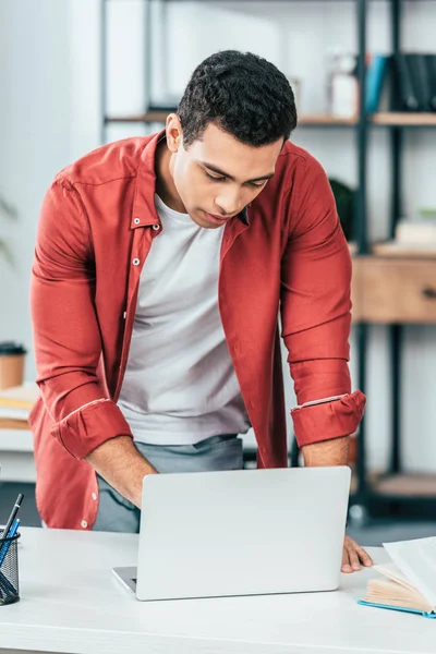 Estudante concentrado em camisa vermelha usando laptop no local de trabalho — Fotografia de Stock