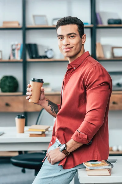 Estudiante en camisa roja sosteniendo una taza de café de papel - foto de stock