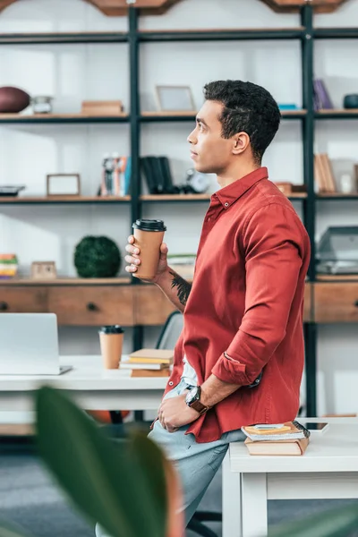 Vue latérale de l'étudiant en chemise rouge tenant une tasse de café en papier — Photo de stock