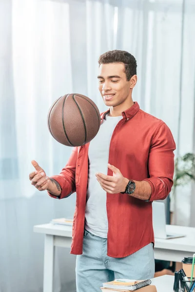 Улыбающаяся брюнетка молодой человек в красной рубашке играет с баскетбольным мячом — стоковое фото