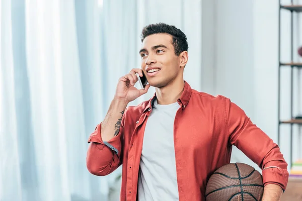 Brunette young man in red shirt with basketball ball talking on smartphone — Stock Photo