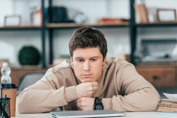 Estudiante triste en reloj de pulsera sentado con los brazos cruzados cerca de la computadora portátil — Stock Photo