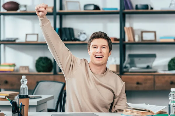 Glücklich lachende Studentin sitzt am Tisch und zeigt Ja-Geste — Stockfoto