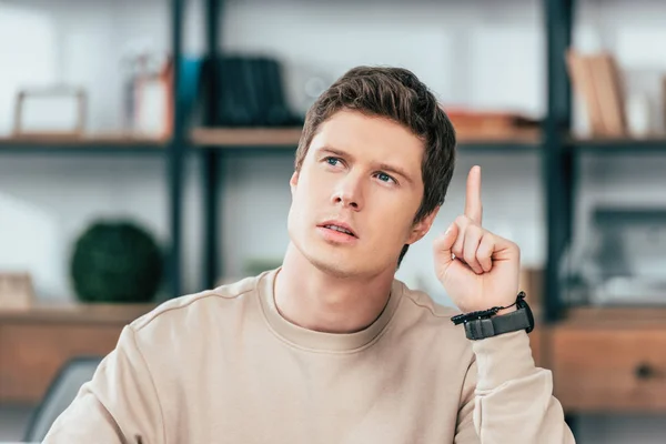 Étudiant pensif dans la montre-bracelet regardant vers le haut et pointant du doigt — Photo de stock