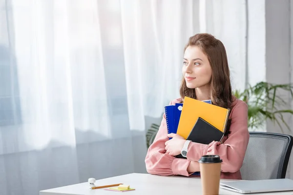 Atractivo estudiante de camisa rosa sosteniendo cuadernos con sonrisa - foto de stock