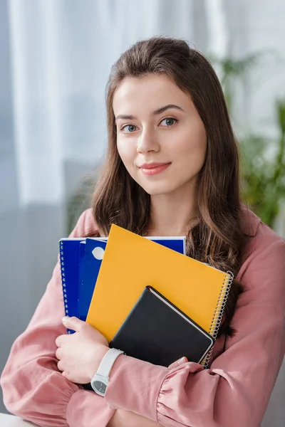 Attractive student in pink shirt holding notebooks with smile — Stock Photo