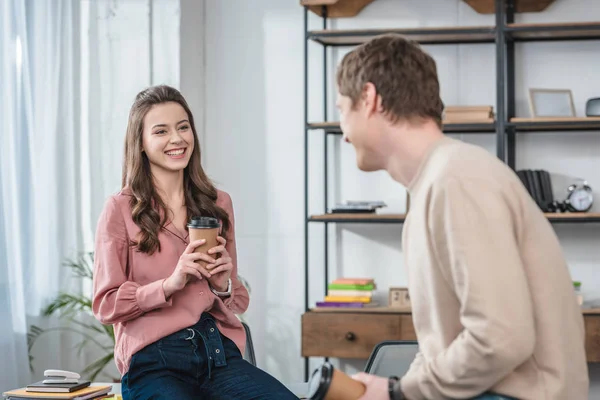 Due amici sorridenti che tengono in mano tazze di carta di caffè e si guardano — Foto stock