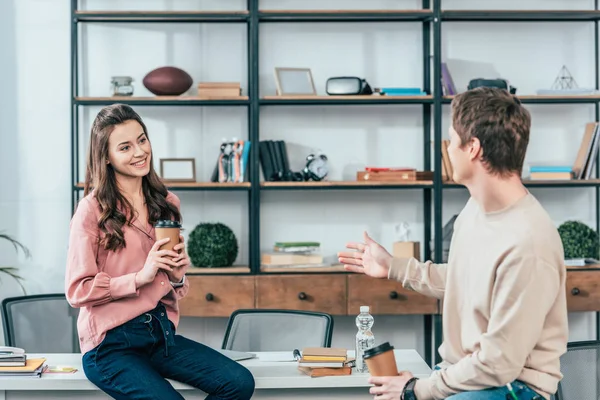 Two smiling friends holding paper cups of coffee and looking at each other — Stock Photo