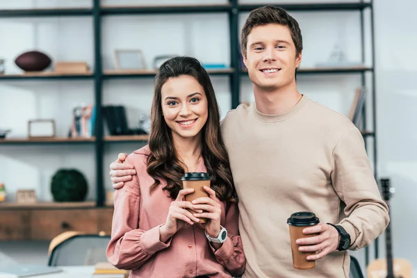Zwei lächelnde Freunde, die Pappbecher Kaffee in der Hand halten und in die Kamera schauen — Stockfoto