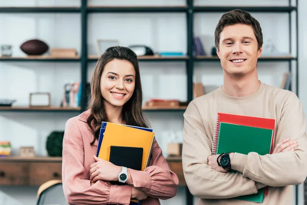 Dos estudiantes sonrientes sosteniendo cuadernos y mirando a la cámara - foto de stock