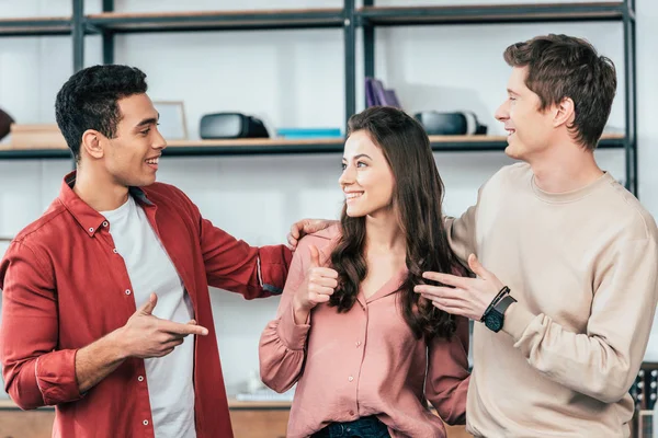 Pretty girl showing thumb up while talking with multiethnic friends — Stock Photo