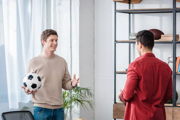 Dos amigos con pelota de fútbol hablando con sonrisa en casa - foto de stock
