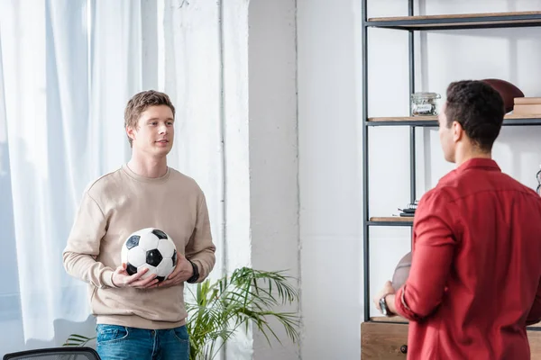 Dos amigos con pelota de fútbol hablando con sonrisa en casa - foto de stock