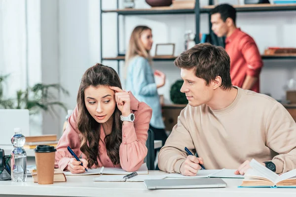 Two students talking and writing in notebooks at table — Stock Photo