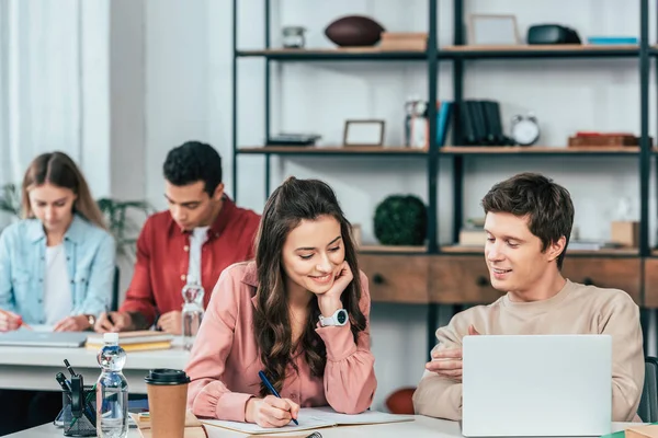 Smiling students sitting at desks and using laptop while studying in classroom — Stock Photo