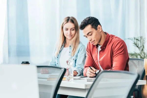 Étudiants multiculturels en vêtements décontractés assis au bureau et étudiant ensemble — Photo de stock