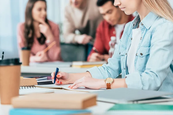 Vista recortada de la escritura de los estudiantes en cuaderno en el aula - foto de stock