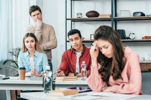 Preoccupato studenti multietnici seduti a tavola e guardando triste ragazza bruna — Foto stock